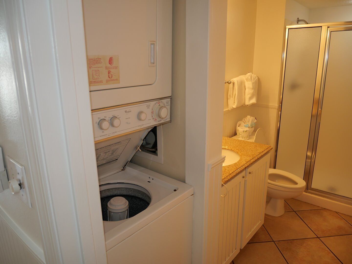 Une salle de bain compacte équipée d’un lave-linge et d’un sèche-linge intégrés, de toilettes et d’un espace douche.