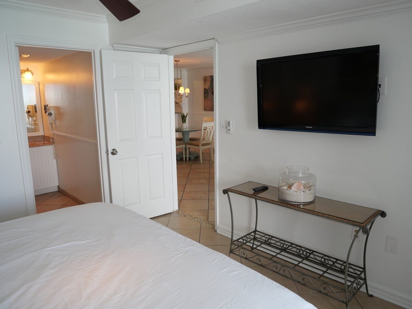 A hotel room with a bed, a TV mounted on the wall, and a small table with a vase.