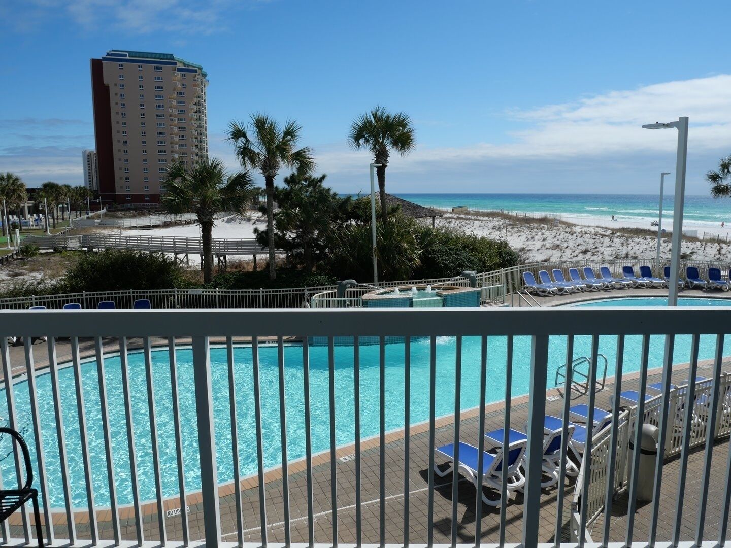 A pool area with a view of the beach, palm trees, and a tall building in the background.