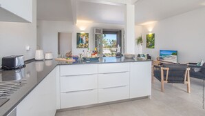A modern kitchen with a central island, white cabinetry, and a dining area with a TV and seating. - Beachside Starfish (Sainte-Anne)