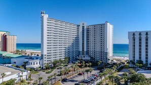 Ein Hochhaus-Hotel mit mehreren Etagen, einem Parkplatz und Blick auf den Strand.