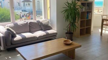 A living room with a sofa, a coffee table, a bookshelf, and a potted plant.