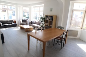 A spacious living room with a wooden dining table, a sofa, and a bookshelf.