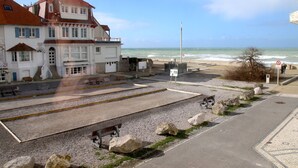 A coastal building with a balcony overlooking the sea, a paved area with benches, and a clear sky. - Duplex 5 persons seaside. (Wissant)
