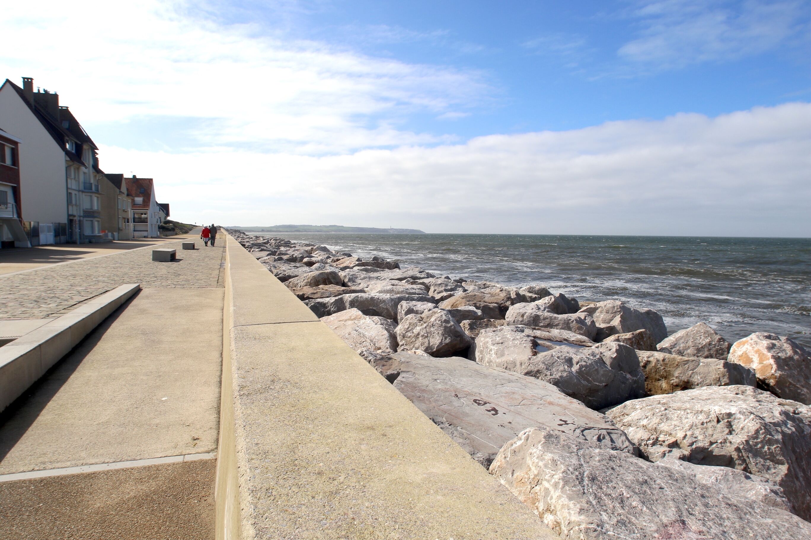 Un paseo marítimo con un camino de hormigón, grandes rocas y edificios a lo largo de la costa.