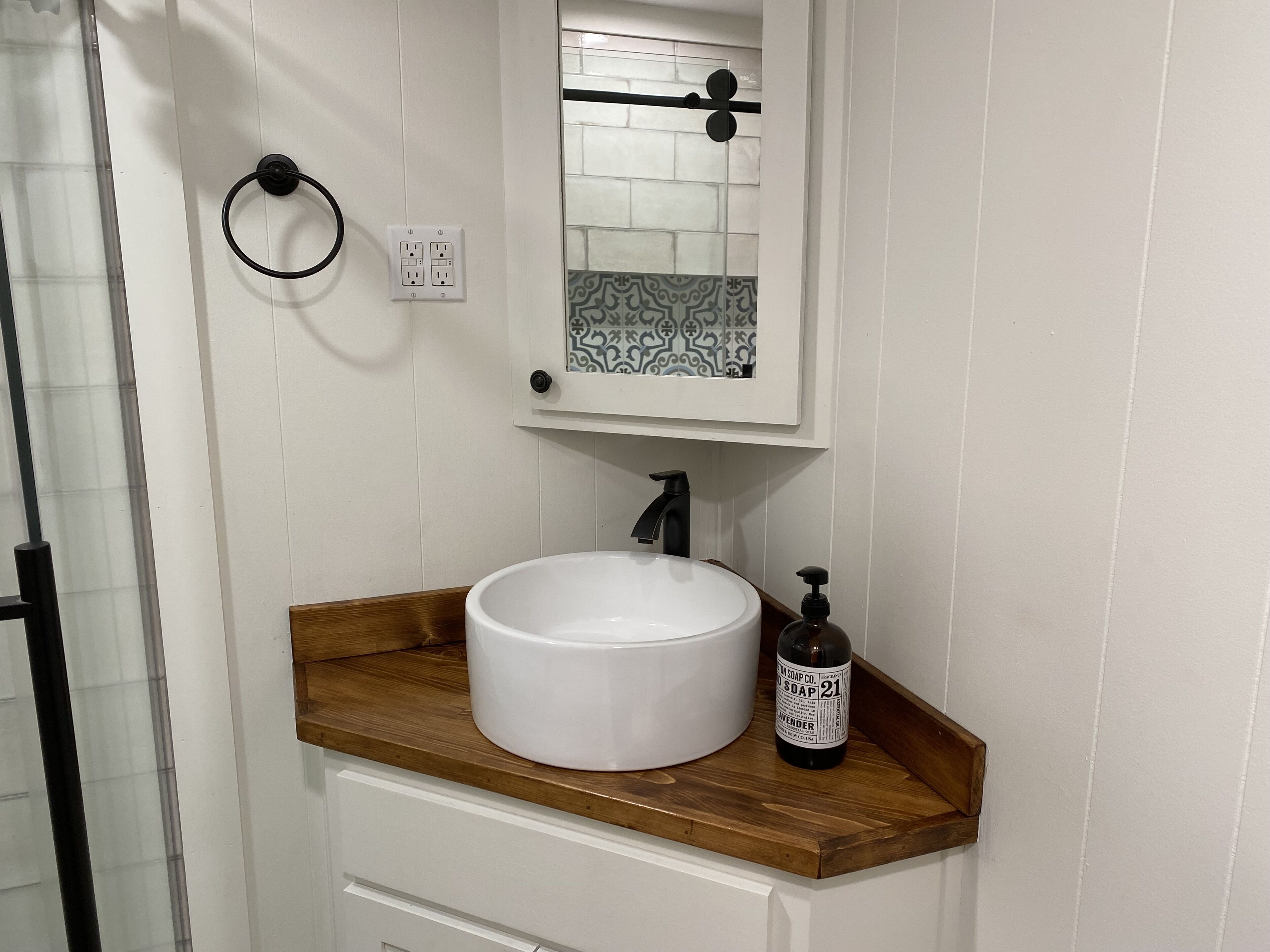 Une salle de bain avec un lavabo blanc, un plan de toilette en bois et un miroir au-dessus.