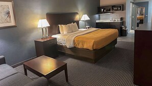 A hotel room with a bed, two bedside tables with lamps, a small table, a sofa, a kitchenette, and a bathroom. - Suburban Studios Montpelier (Montpelier)