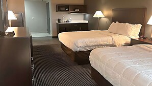 A hotel room with two beds, a desk, a chair, a microwave, a sink, and two lamps. - Suburban Studios Montpelier (Montpelier)