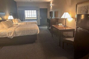 A hotel room with two beds, a desk, a chair, a TV, and a refrigerator. - Suburban Studios Montpelier (Montpelier)