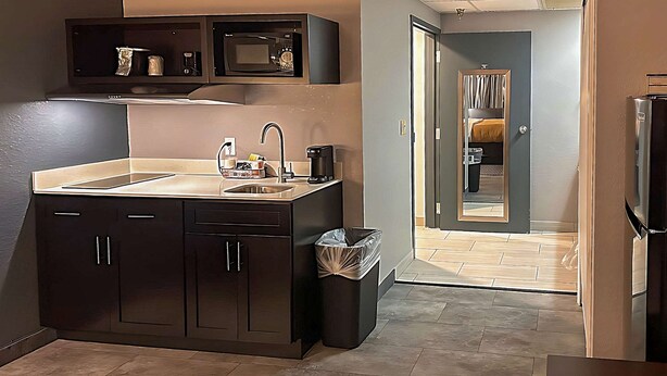 A modern kitchen with dark cabinets, a stainless steel sink, and a microwave above the counter. - Suburban Studios Montpelier (Montpelier)