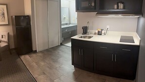 A modern kitchen with dark cabinets, a stainless steel sink, and a built-in microwave. - Suburban Studios Montpelier (Montpelier)