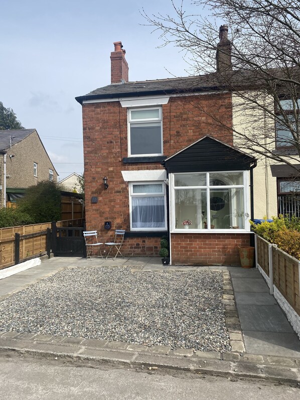 A two-story brick house with a front garden, a wooden gate, and a small seating area with a chair and a table. - 2 Bedroom Cute & Cosy Cottage in the village of Adlington, Lancashire (Adlington)