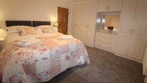 A bedroom with a large bed, a nightstand, a dresser, and a wardrobe.