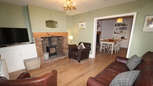 A living room with a fireplace, leather sofas, a television, and a dining area in the background.