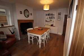 A dining area with a wooden table and white chairs, a fireplace, a bookshelf, and a hanging light fixture. - 2 Bedroom Cute & Cosy Cottage in the village of Adlington, Lancashire (Adlington)