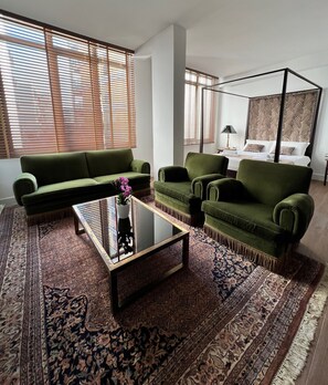 A modern living room with a green sofa set, a glass coffee table, and a large patterned rug.