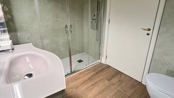 Une salle de bain moderne avec une douche à parois de verre, un lavabo blanc et des toilettes.