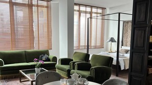 Ett modernt vardagsrum med en grön soffa, ett runt matbord med stolar och en säng med ett mönstrat sänggavel.