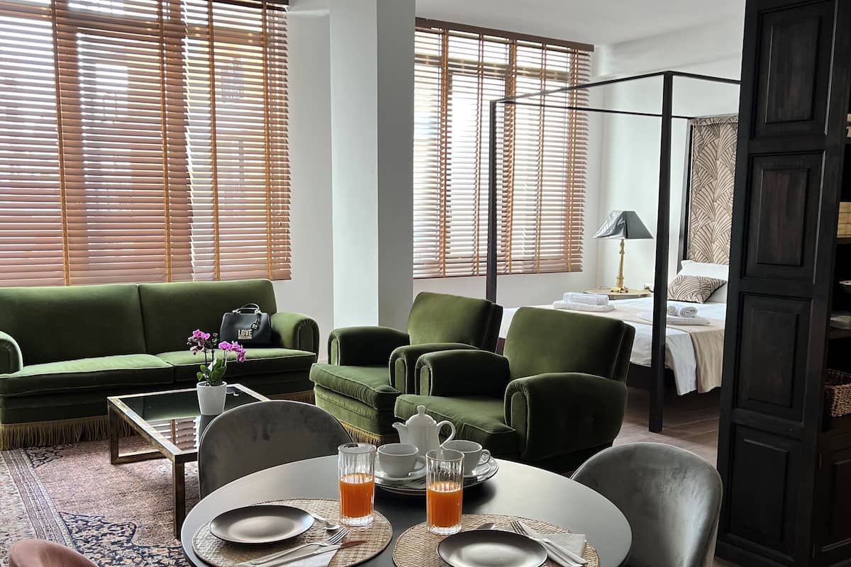 Una sala de estar moderna con un sofá verde, una mesa de comedor redonda con sillas, y una cama con cabecera estampada.