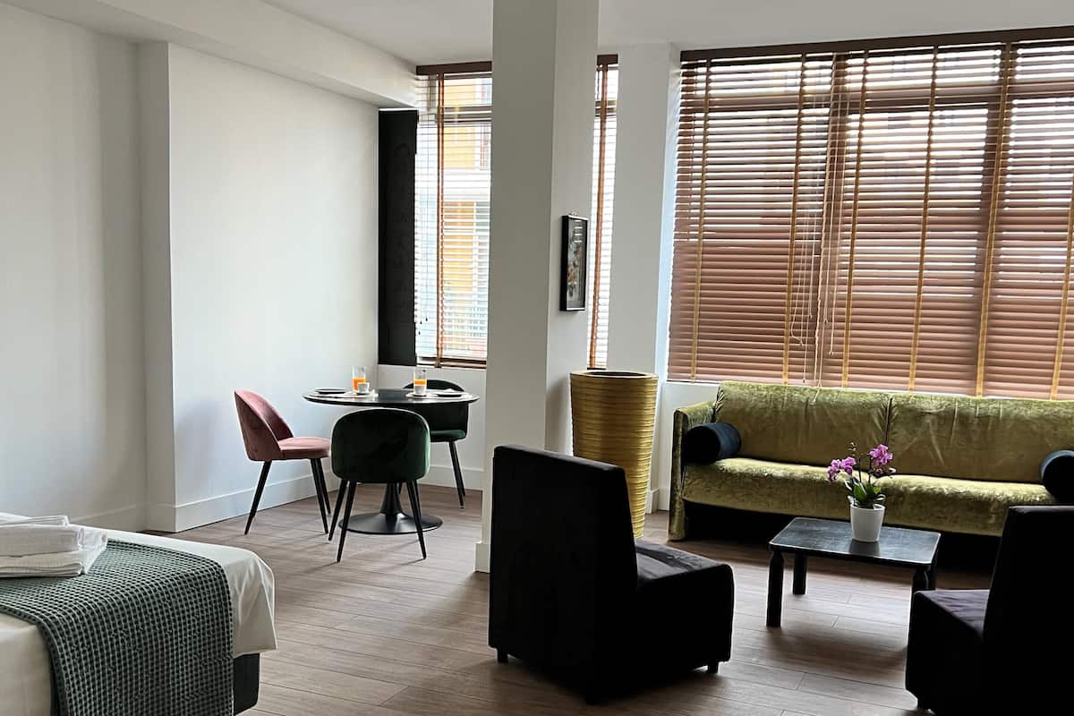Una habitación de hotel moderna con una cama, un sofá verde, una mesa de comedor con dos sillas y una pequeña mesa de centro.