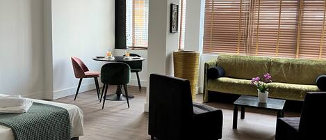 A modern hotel room with a bed, a green sofa, a dining table with two chairs, and a small coffee table.