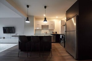 A modern kitchen with a central island, bar stools, stainless steel appliances, and pendant lighting. - Design 3-bedroom flat with private terrace in Little Italy by Denstays (Montréal)