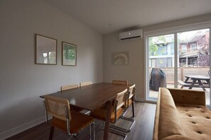 A dining area with a wooden table and chairs, a sofa, and a sliding glass door leading to an outdoor patio.