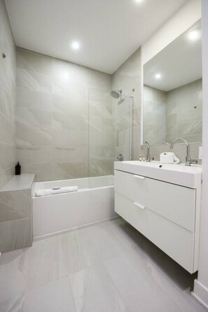 A modern bathroom with a bathtub, a shower, a vanity with a mirror, and a toilet.