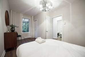 Ein Schlafzimmer mit einem großen Bett, einem Schminktisch, einem Spiegel, einem Fenster und einer Tür zu einem anderen Raum.