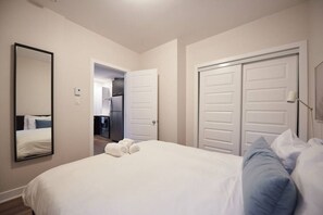 A hotel room with a bed, a large mirror, a wardrobe, and a door leading to a kitchen.