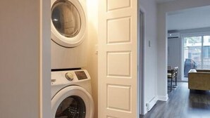 A laundry room with two washing machines, a wooden floor, and a door leading to a living area. - Design 3-bedroom flat with private terrace in Little Italy by Denstays (Montréal)