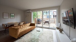 A living room with a sofa, dining table, chairs, and a large sliding glass door leading to an outdoor patio. - Design 3-bedroom flat with private terrace in Little Italy by Denstays (Montréal)