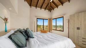 Un dormitorio con una cama grande, techo de madera y vista a un paisaje por la ventana.