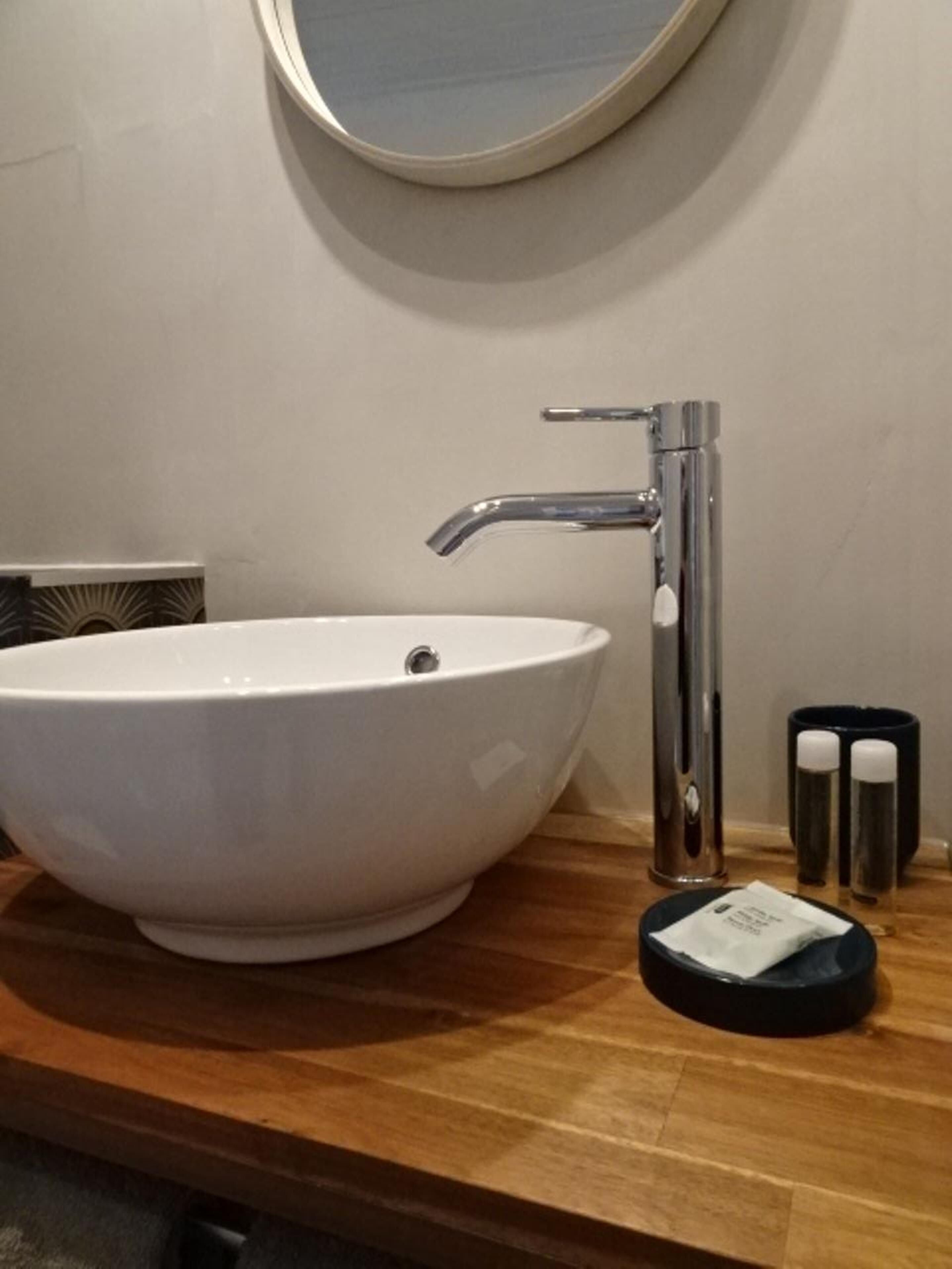 A white vessel sink with a modern faucet, a small black tray with a tissue, and two black containers on a wooden countertop.