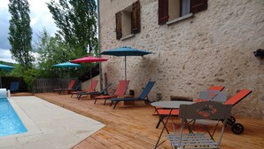 Une terrasse en bois avec une piscine, des chaises longues et des parasols.