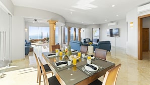 Un vaste espace de vie comprenant un coin repas avec une table préparée pour le petit-déjeuner, un canapé et une vue sur l’océan.