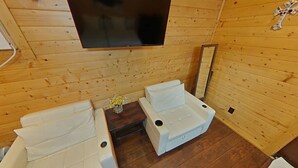 Een houten hut met twee witte banken, een flatscreen-tv en een bijzettafeltje met een bloevas.