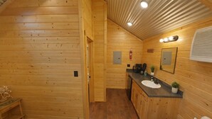 A wooden cabin interior with a bed, a small table, a sink, and a mirror. - Beautiful Log cabin overlooking a meadow (Pipe Creek)