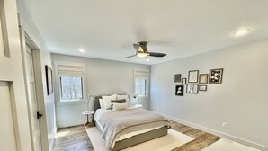 A bedroom with a bed, a ceiling fan, a desk, and framed pictures on the wall. - Beautiful Serene Carriage House Apartment (Spearfish)