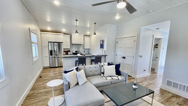 A modern living room with a grey sofa, a glass coffee table, and a dining area in the background. - Beautiful Serene Carriage House Apartment (Spearfish)