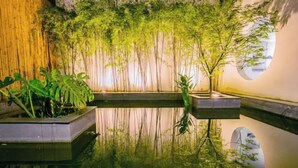 Un jardín interior tranquilo con una fuente acuática reflectante, una pared de bambú y un ventanal circular.