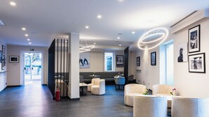 A modern lobby with seating areas, a reception desk, and framed artwork on the walls. - J Maluni City Hotel (Rome)