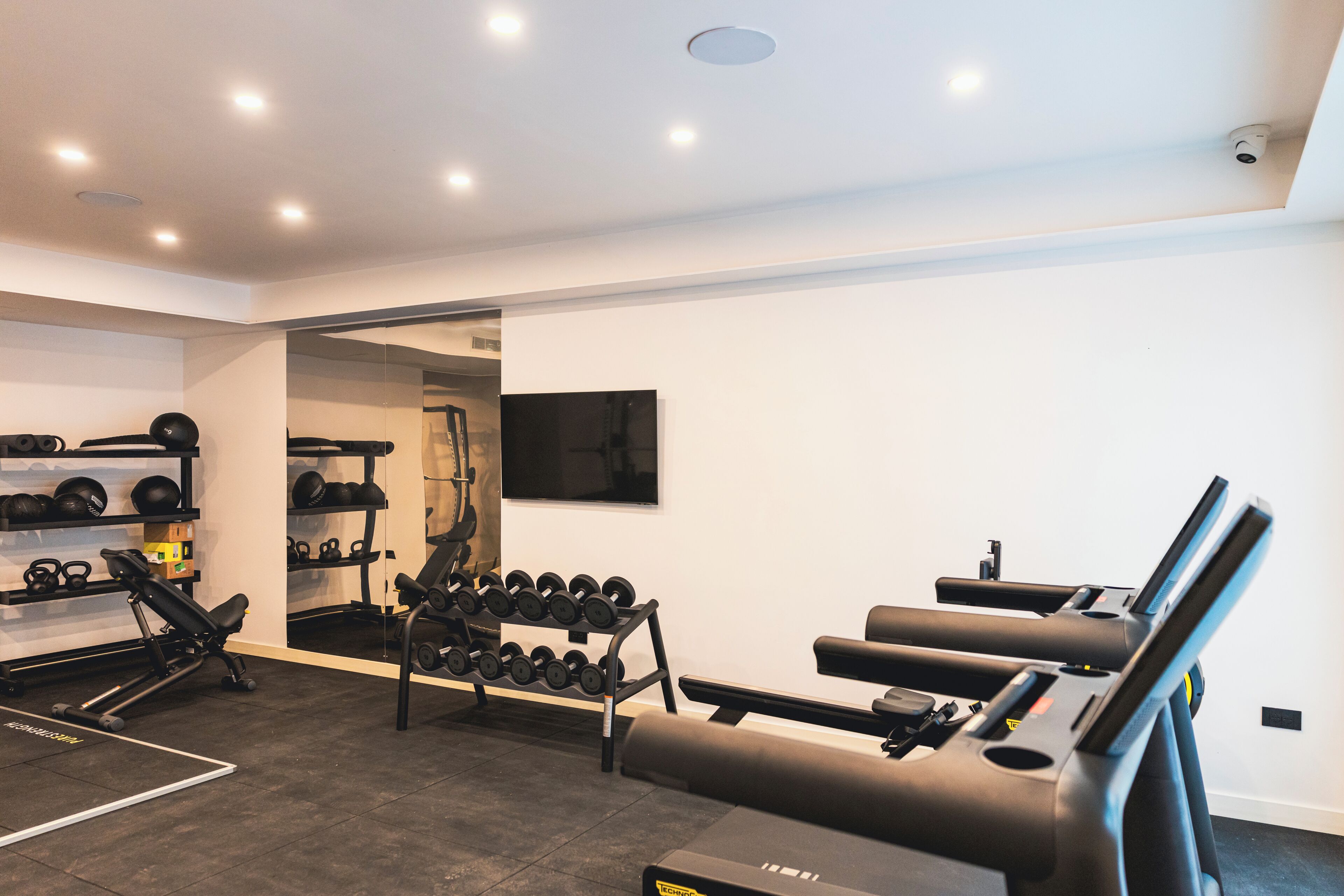 Et moderne fitnesscenter med træningsudstyr, et spejl og et fjernsyn.