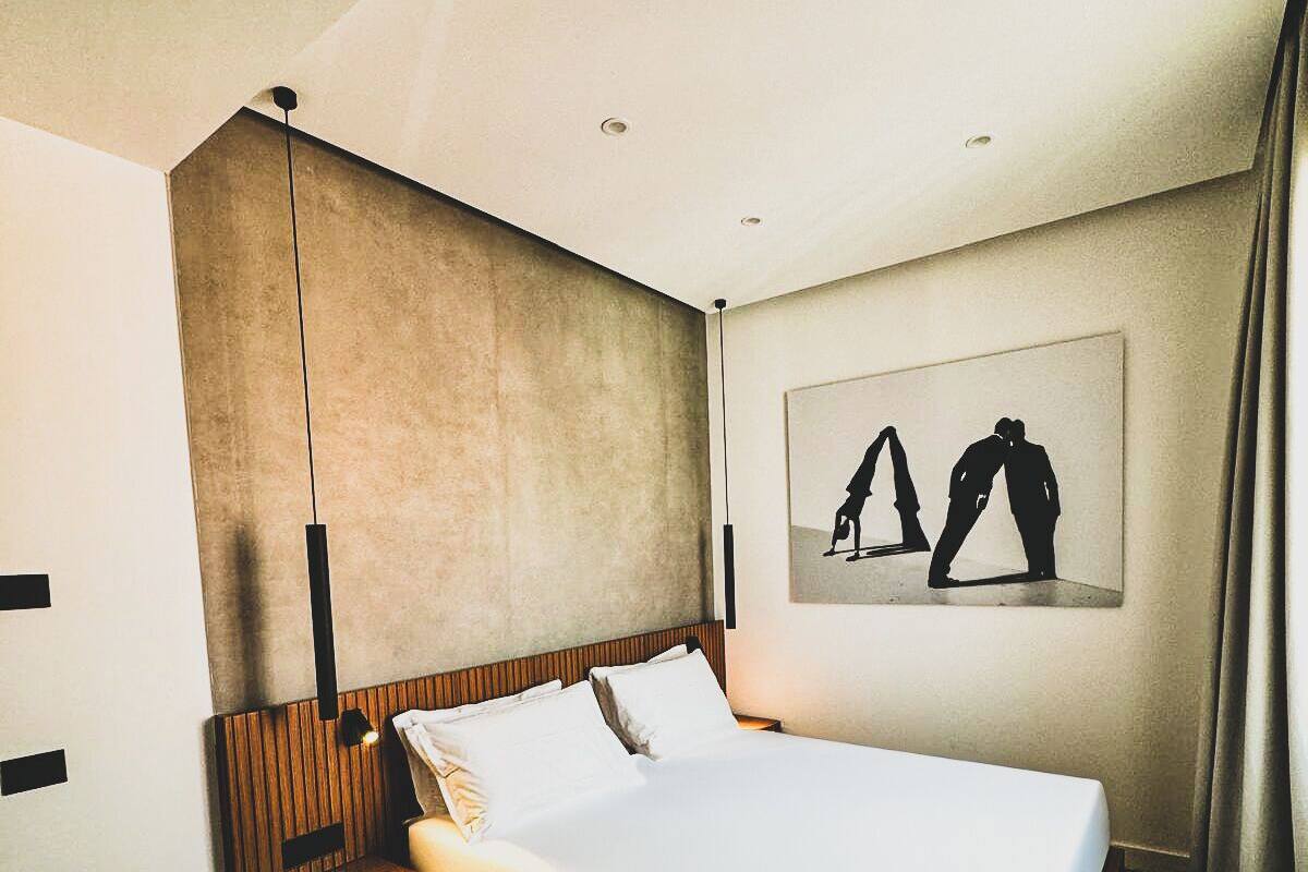Una habitació d'hotel moderna amb un llit gran, un panell de fusta al capçal i una obra d'art penjada a la paret que representa dues figures.