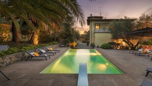 A rectangular swimming pool with a diving board in the center, surrounded by lounge chairs and a stone wall. - Villa Gaius 8+2, Emma Villas (Rosignano Marittimo)