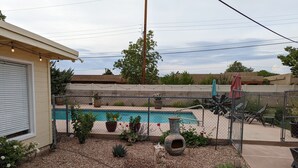 Un jardin avec une piscine, entouré d’une clôture, agrémenté de plantes en pot et de meubles d’extérieur.