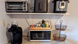 Une cuisine équipée d’un grille-pain, d’un four à micro-ondes, d’une machine à café et d’un panier métallique à deux niveaux posé sur le plan de travail.
