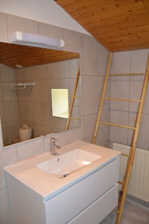 Une salle de bain avec un lavabo blanc, un miroir et un plafond en bois.