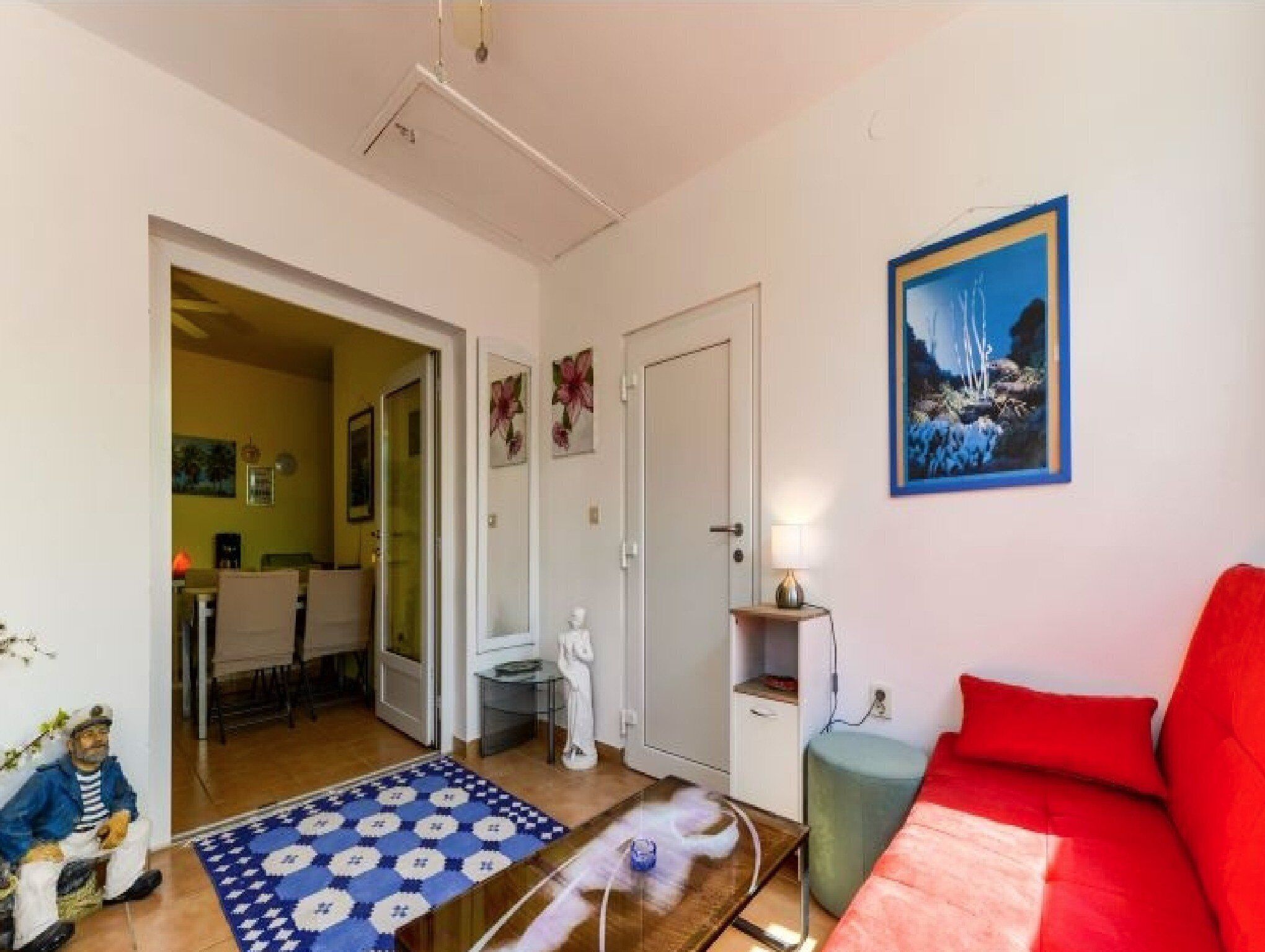 A room with a red sofa, a painting of a waterfall, a small table with a lamp, and a patterned rug.