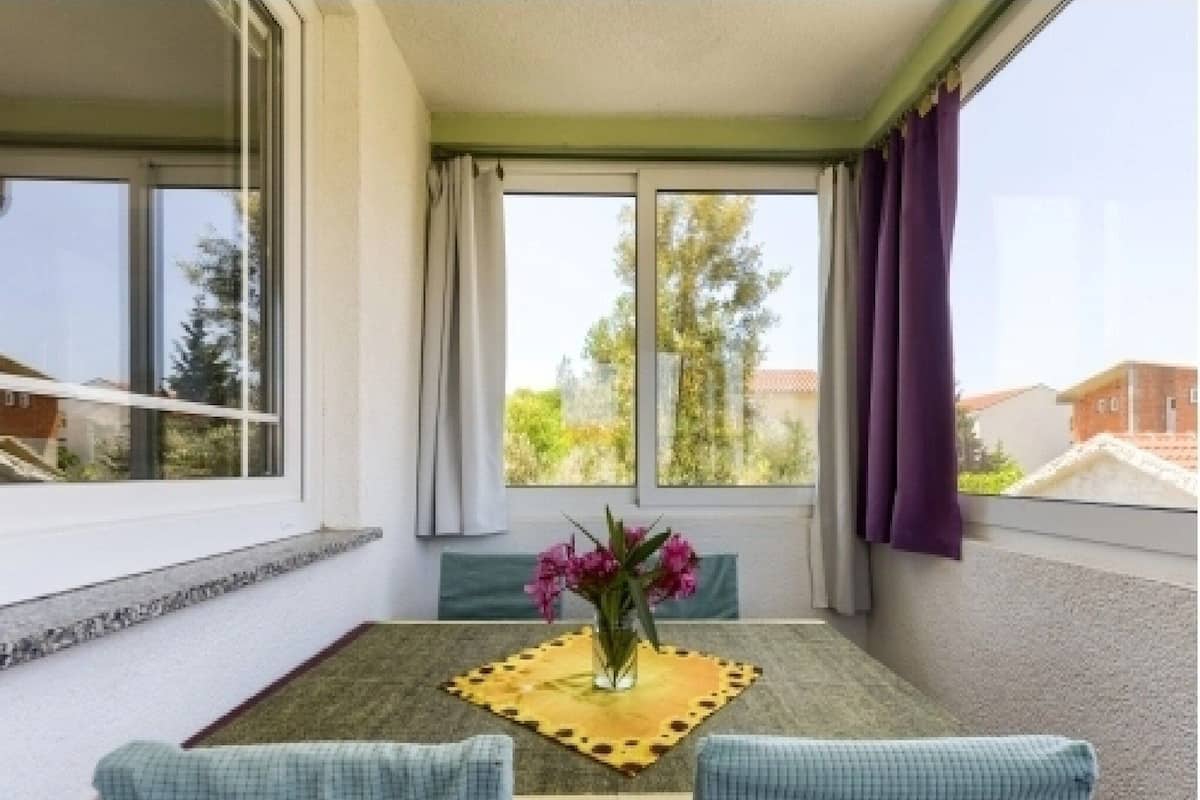 A balcony with a table, chairs, and a vase of flowers.